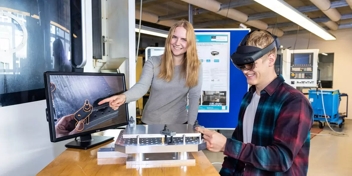 Zwei Studierende befinden sich im Labor. Student sichtet Teil mit AR-Brille. Studentin deutet auf angeschlossenen Bildschirm.